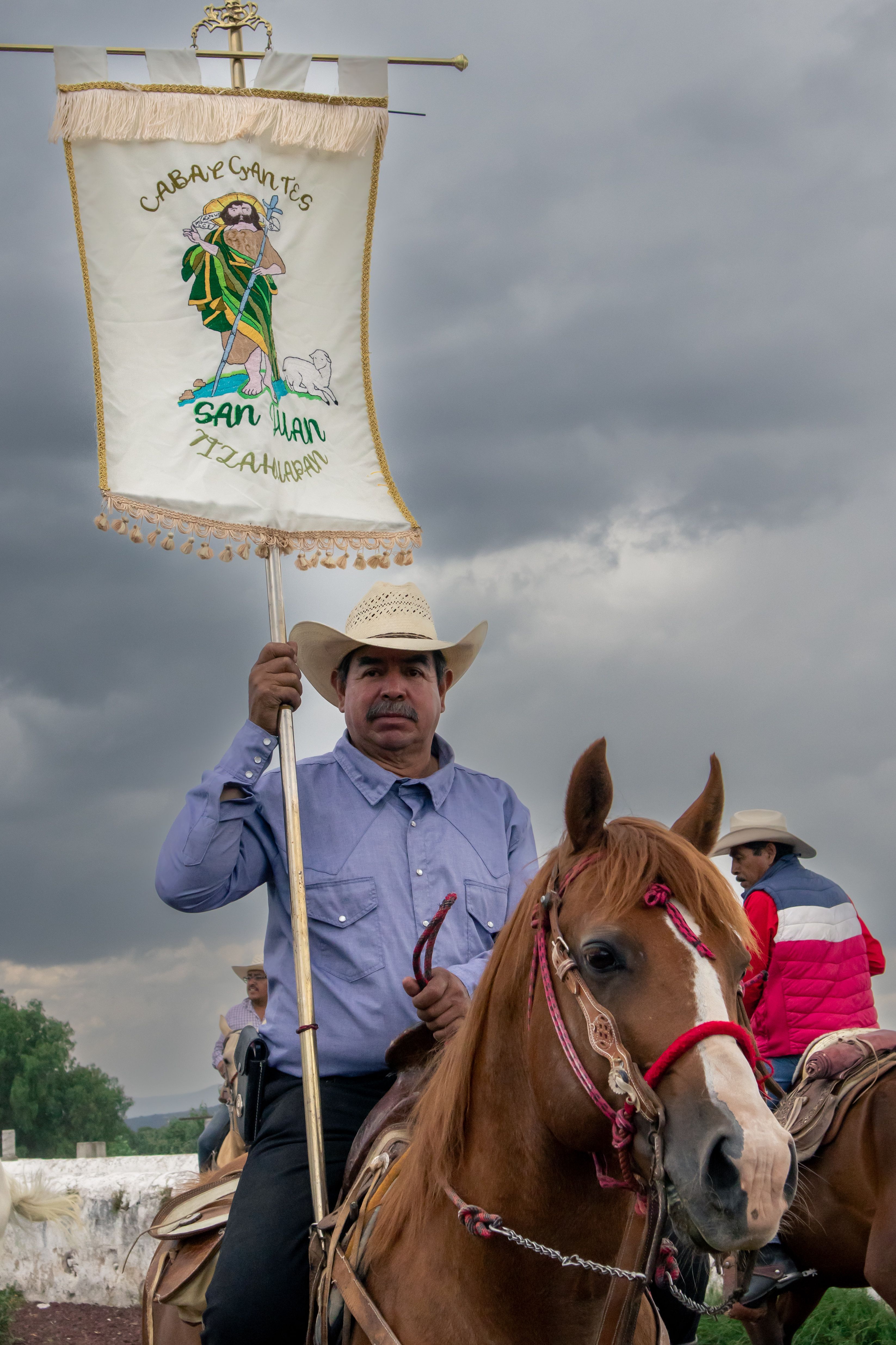 Man on horseback holding a religious banner during cultural event.