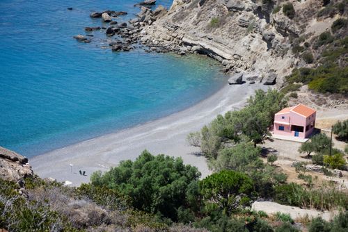 Free Aerial view of a serene beach with turquoise waters and a quaint pink house by the shore. Stock Photo