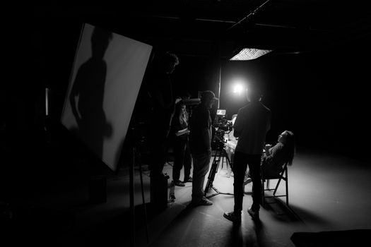 A black and white view of a film crew working on set with dramatic lighting.