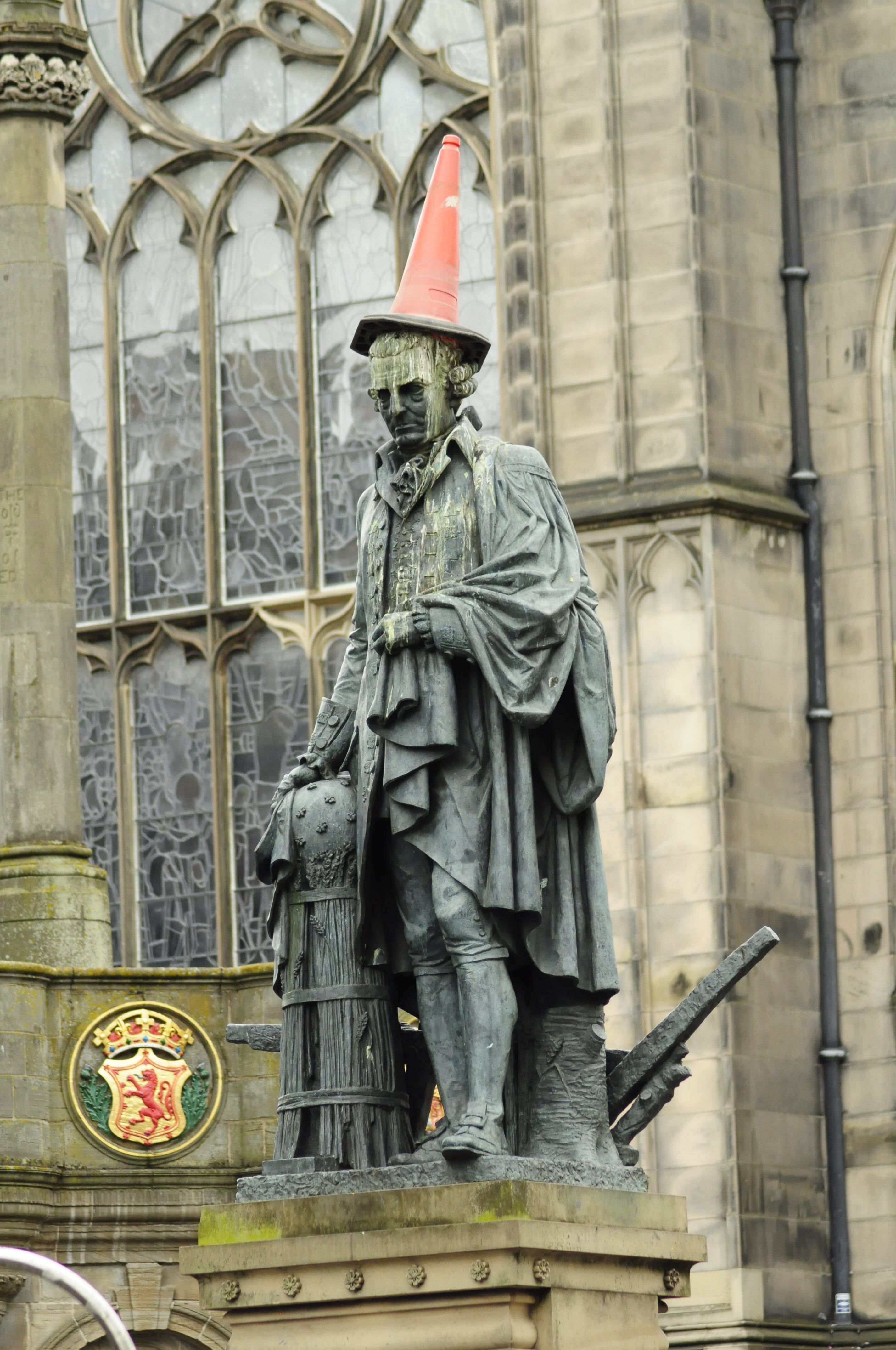 Bronze statue in Edinburgh humorously adorned with a traffic cone hat.