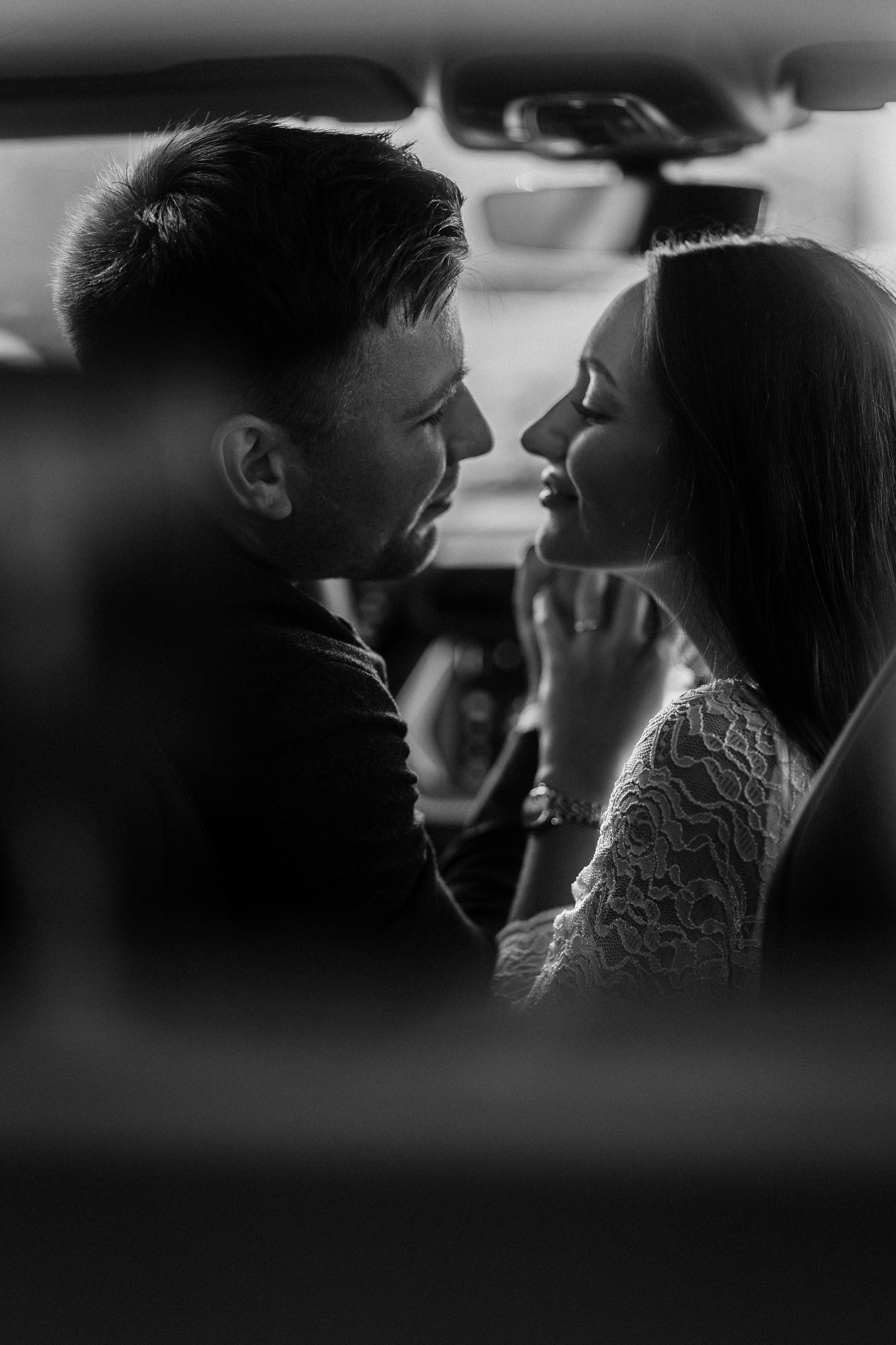 A tender black and white portrait of a couple sharing a romantic moment inside a car.