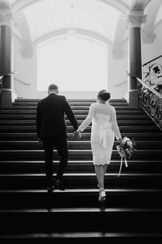 A couple in wedding attire holding hands as they ascend a grand staircase indoors.