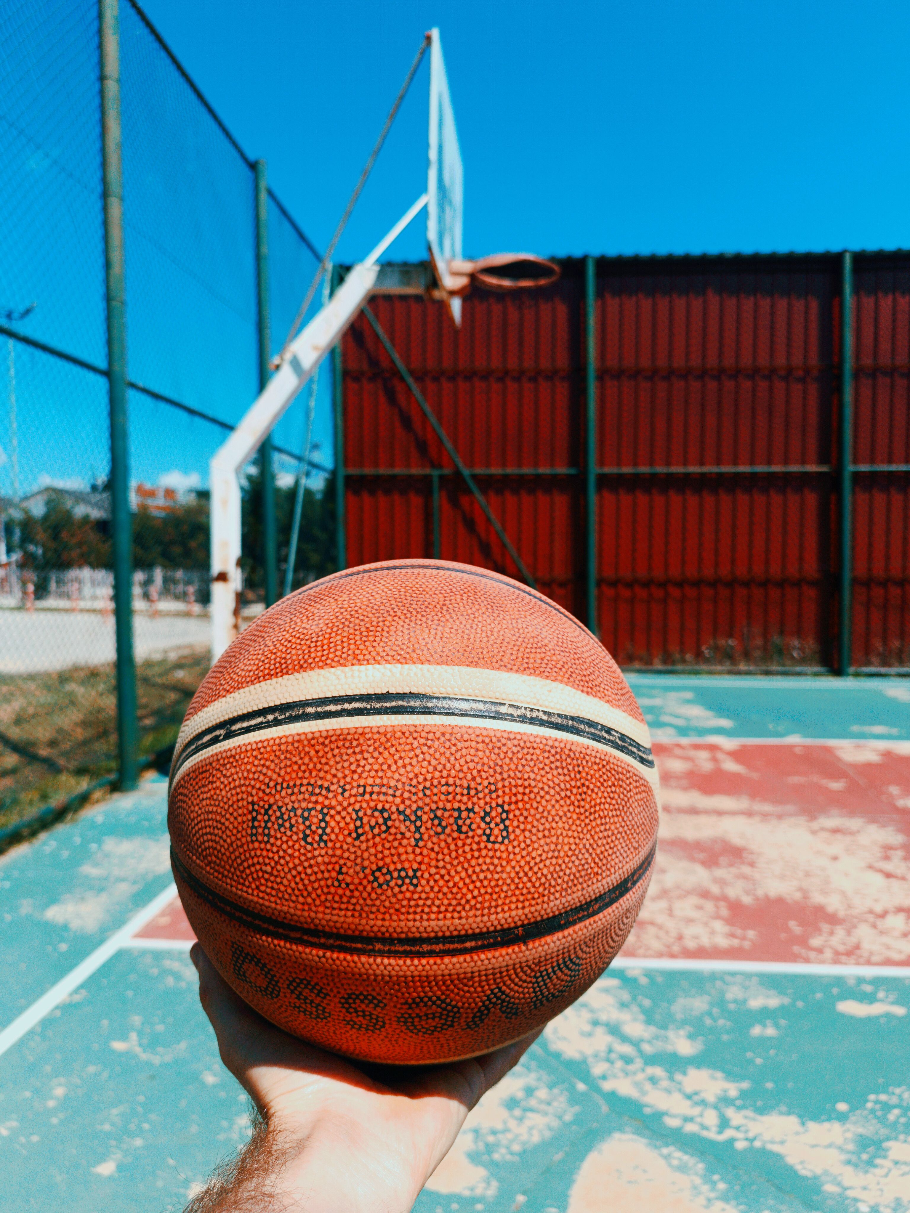 Close-up of a basketball held by a person on an outdoor court on a sunny day.