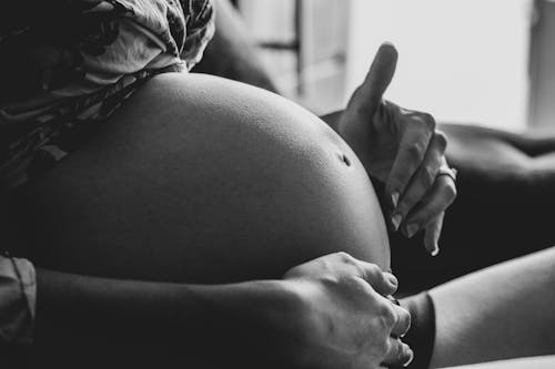 Free Crop pregnant woman touching belly belly while resting on couch Stock Photo