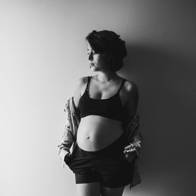 Retrato em preto e branco de mulher grávida em pé, mãos nos bolsos