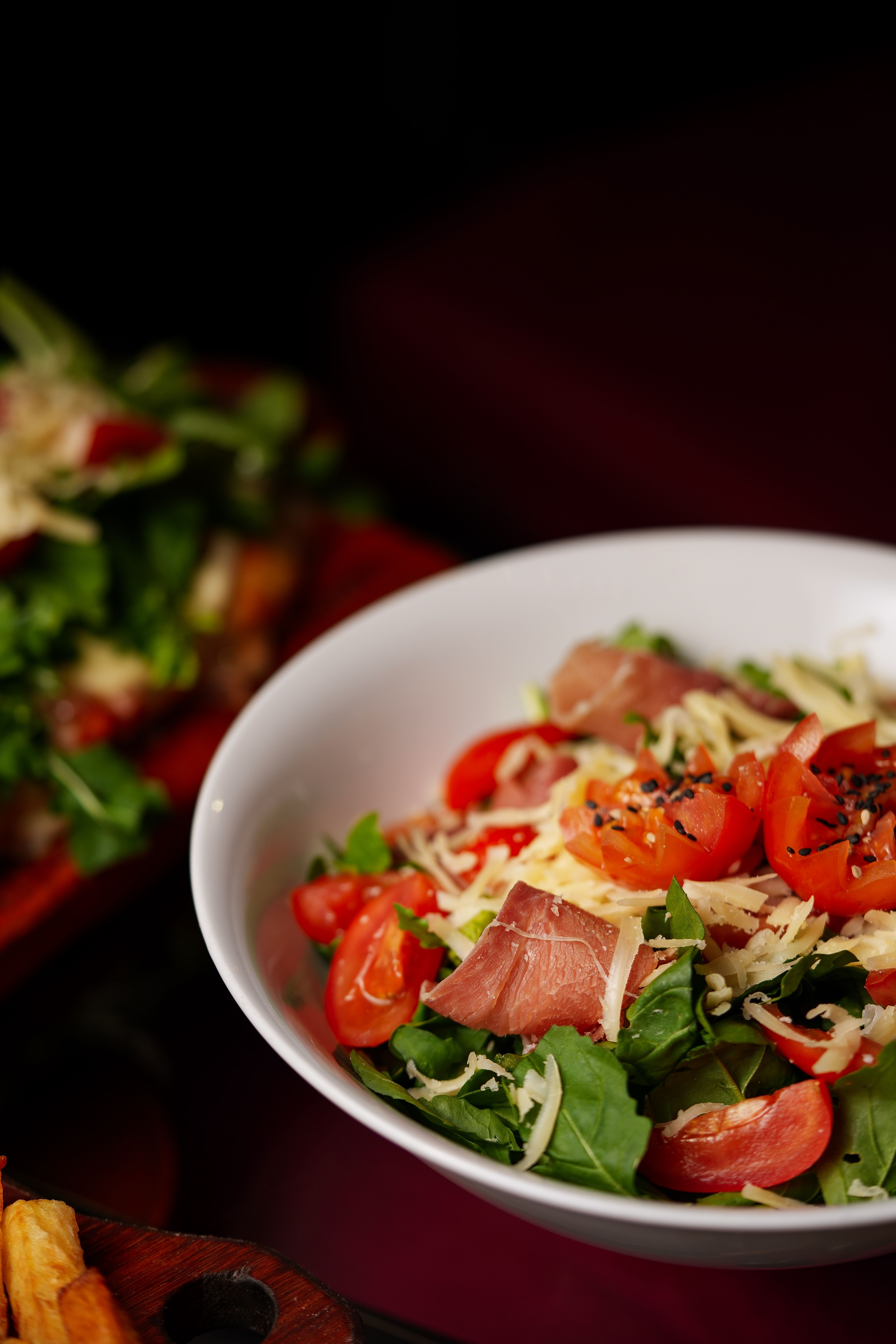 Delicious salad with cherry tomatoes, prosciutto, cheese, and mixed greens in a white bowl.