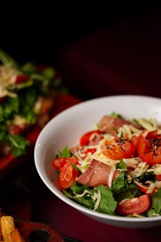 Delicious salad with cherry tomatoes, prosciutto, cheese, and mixed greens in a white bowl.