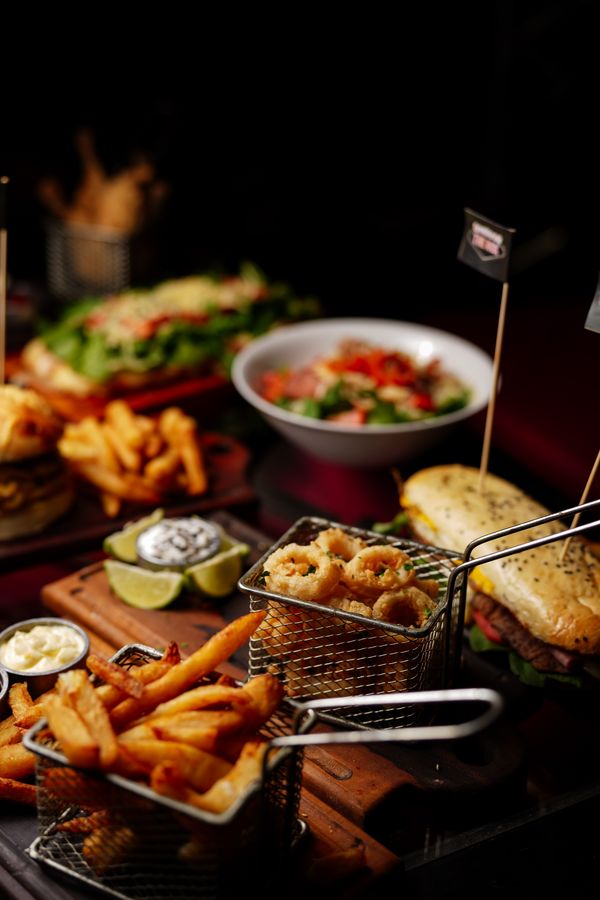 Espalhamento de fast food gourmet com batatas fritas, sanduíche e salada em uma mesa de madeira.