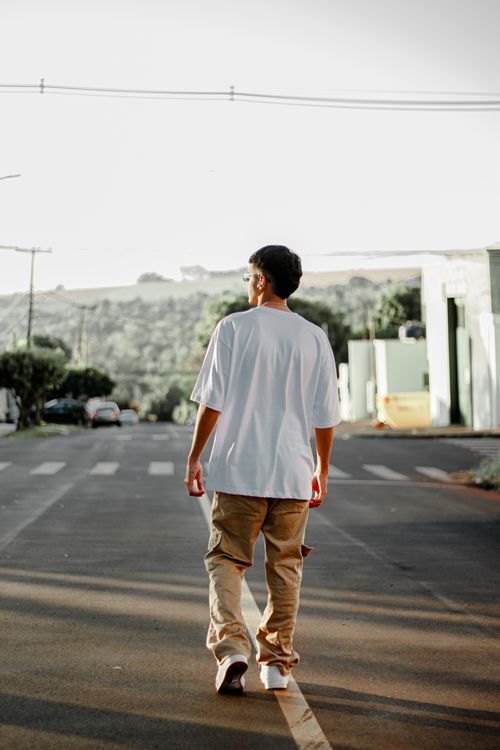 Free A young adult walks across a city street during sunset, capturing a serene moment outdoors. Stock Photo