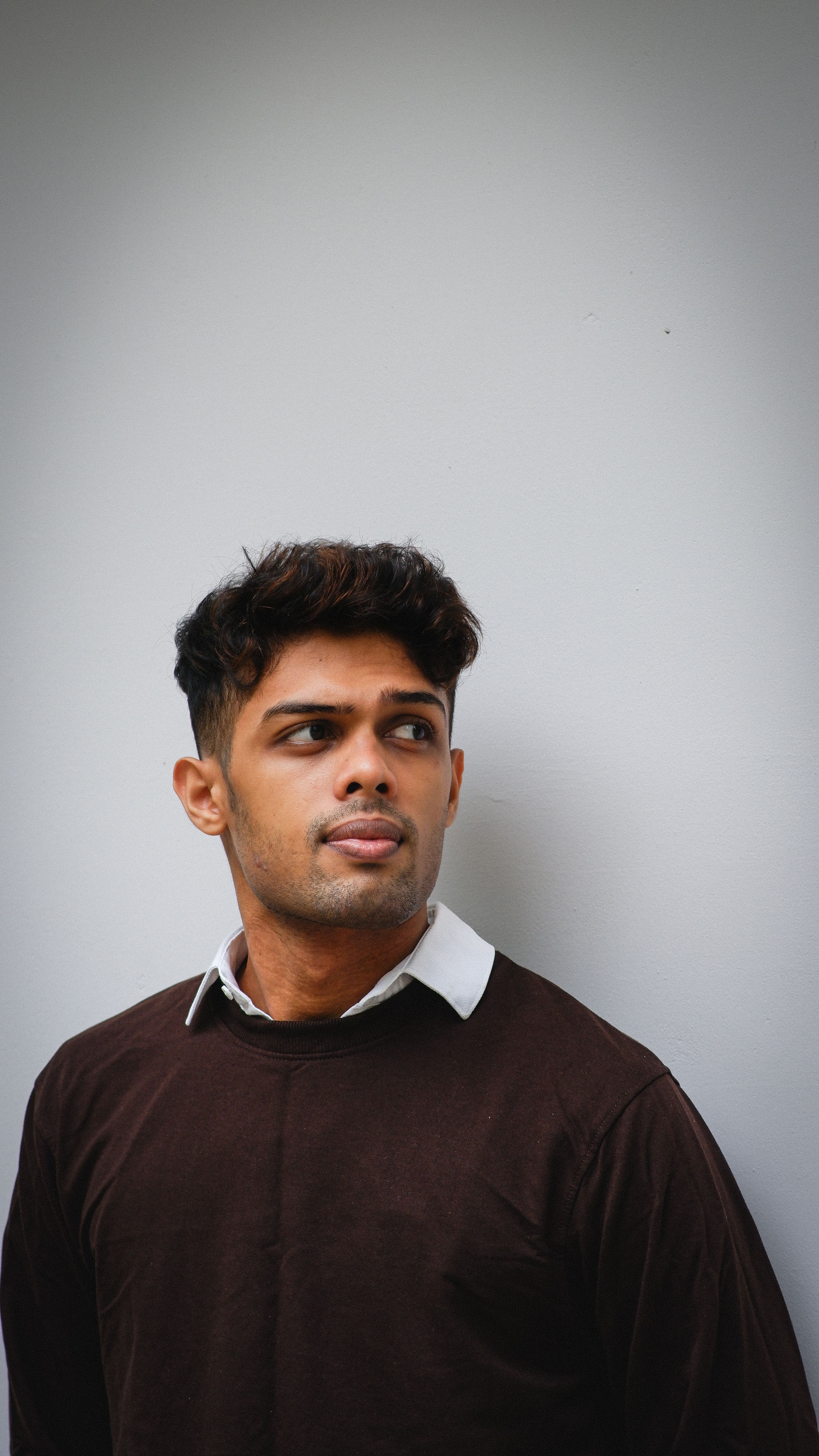 Stylish young man posing confidently against a minimalist white wall.