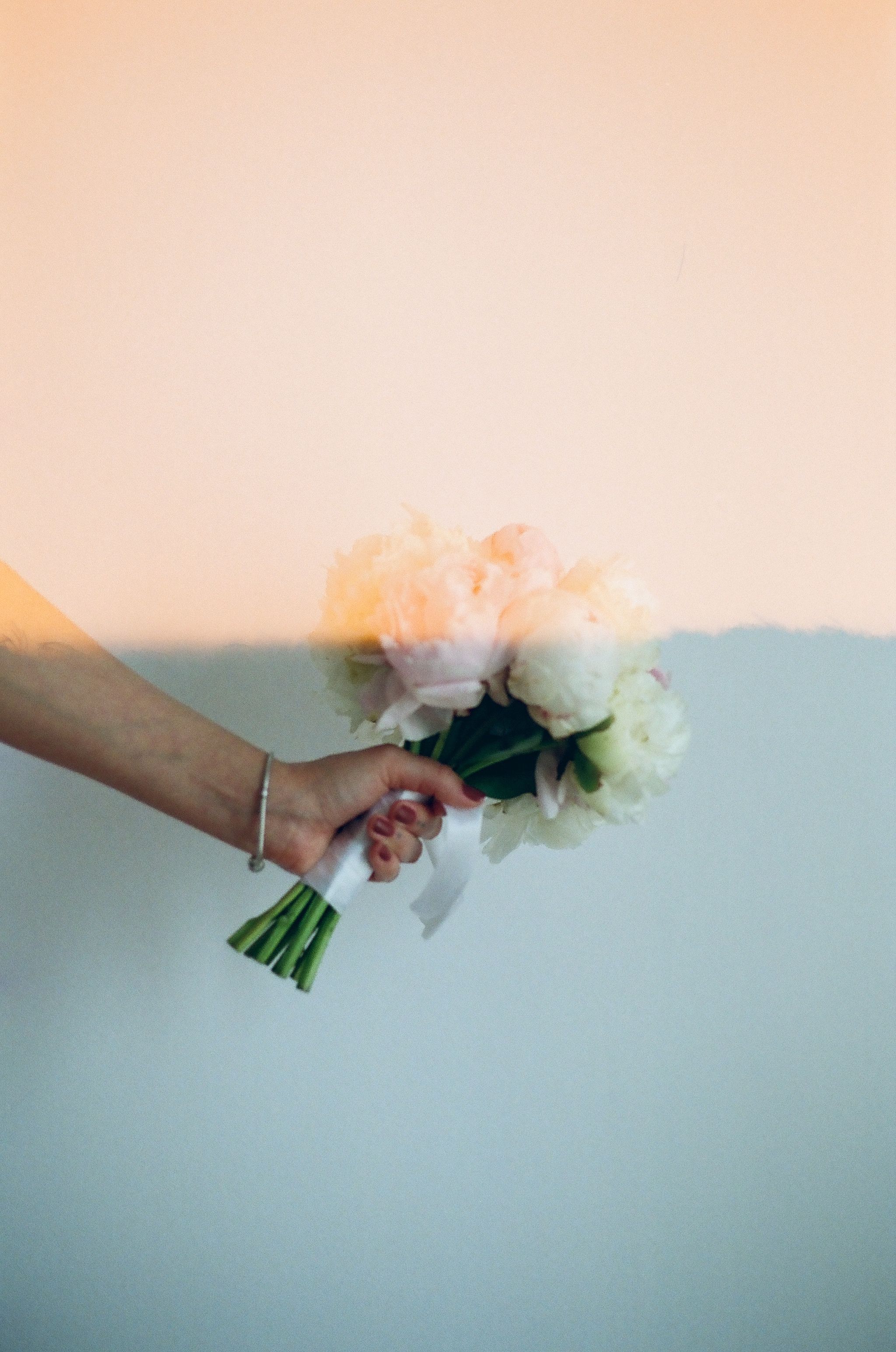 A hand holding a bouquet of flowers against a pastel wall, creating a soft and artistic visual.