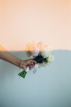 A hand holding a bouquet of flowers against a pastel wall, creating a soft and artistic visual.
