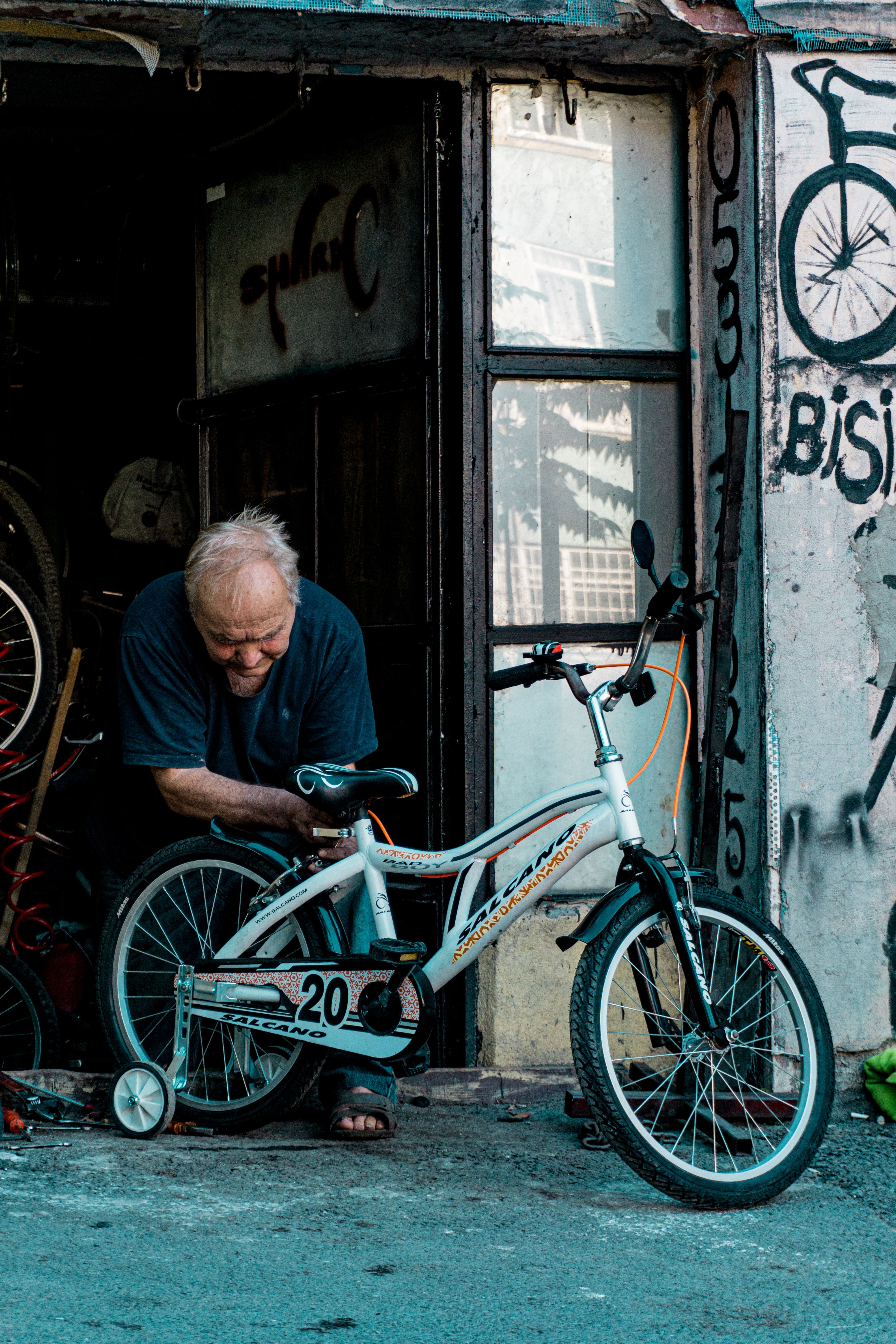 An elderly man repairing a white bicycle outside a workshop in Istanbul.