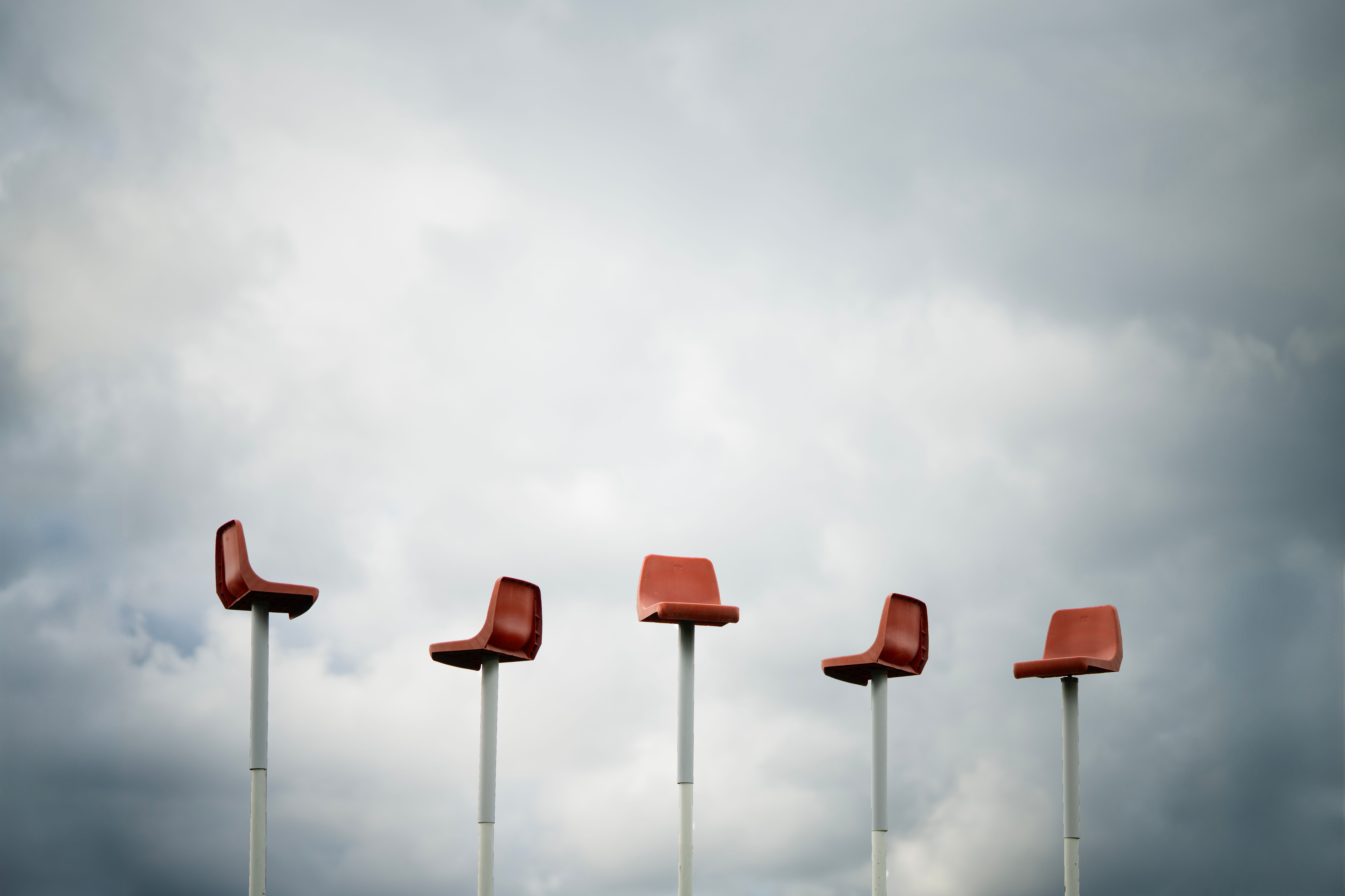 A row of elevated red chairs set dramatically against a cloudy sky, evoking a surreal atmosphere.