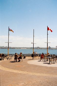 Scenic view of waterfront dining area featuring Canadian and British Columbia flags on a sunny day.