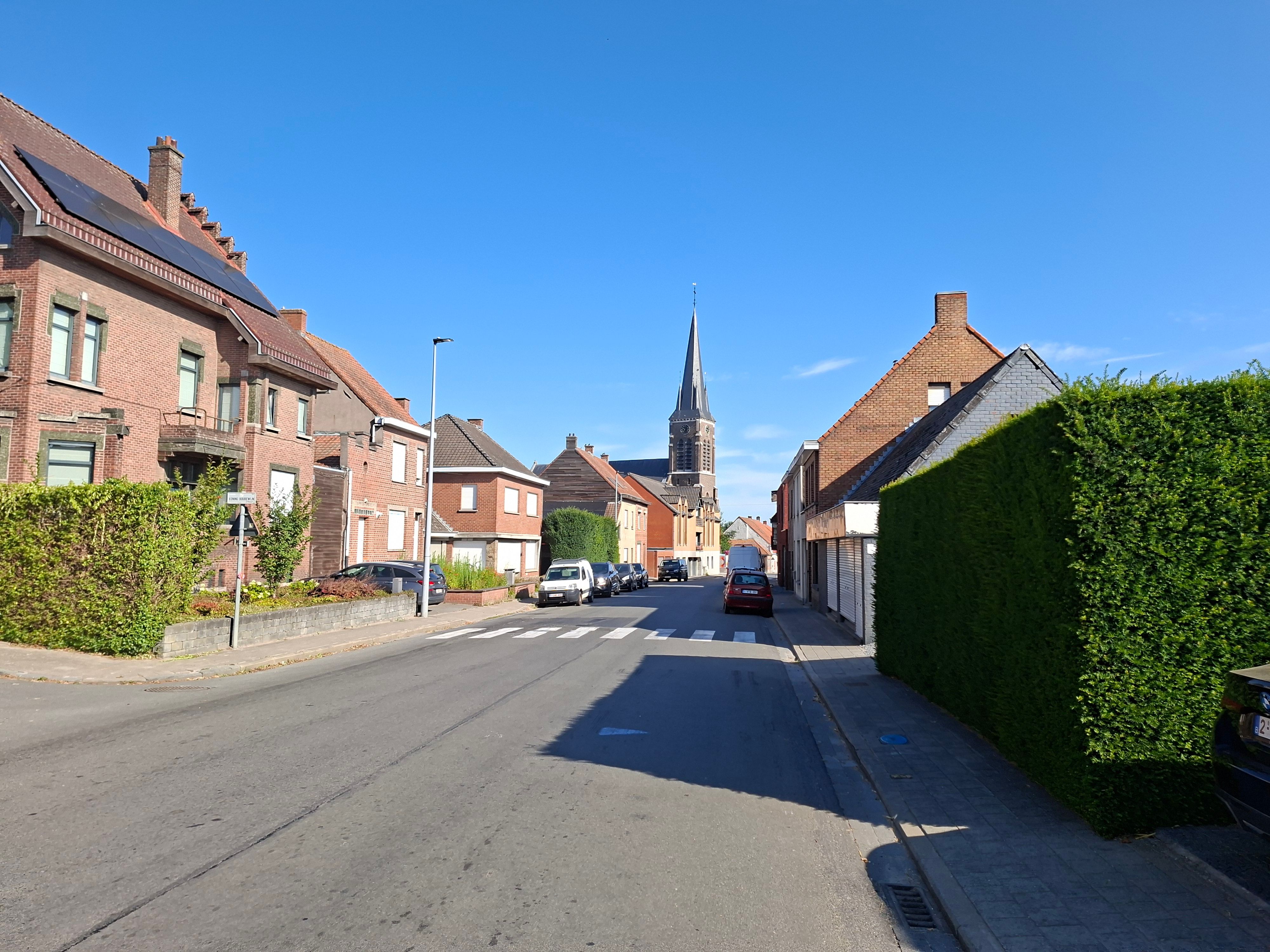 A picturesque street in Belgium featuring a historic church spire under a clear blue sky.