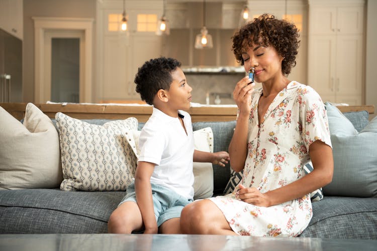 A Young Boy Looking At His Mother Smelling A Bottle While Sitting On The Couch