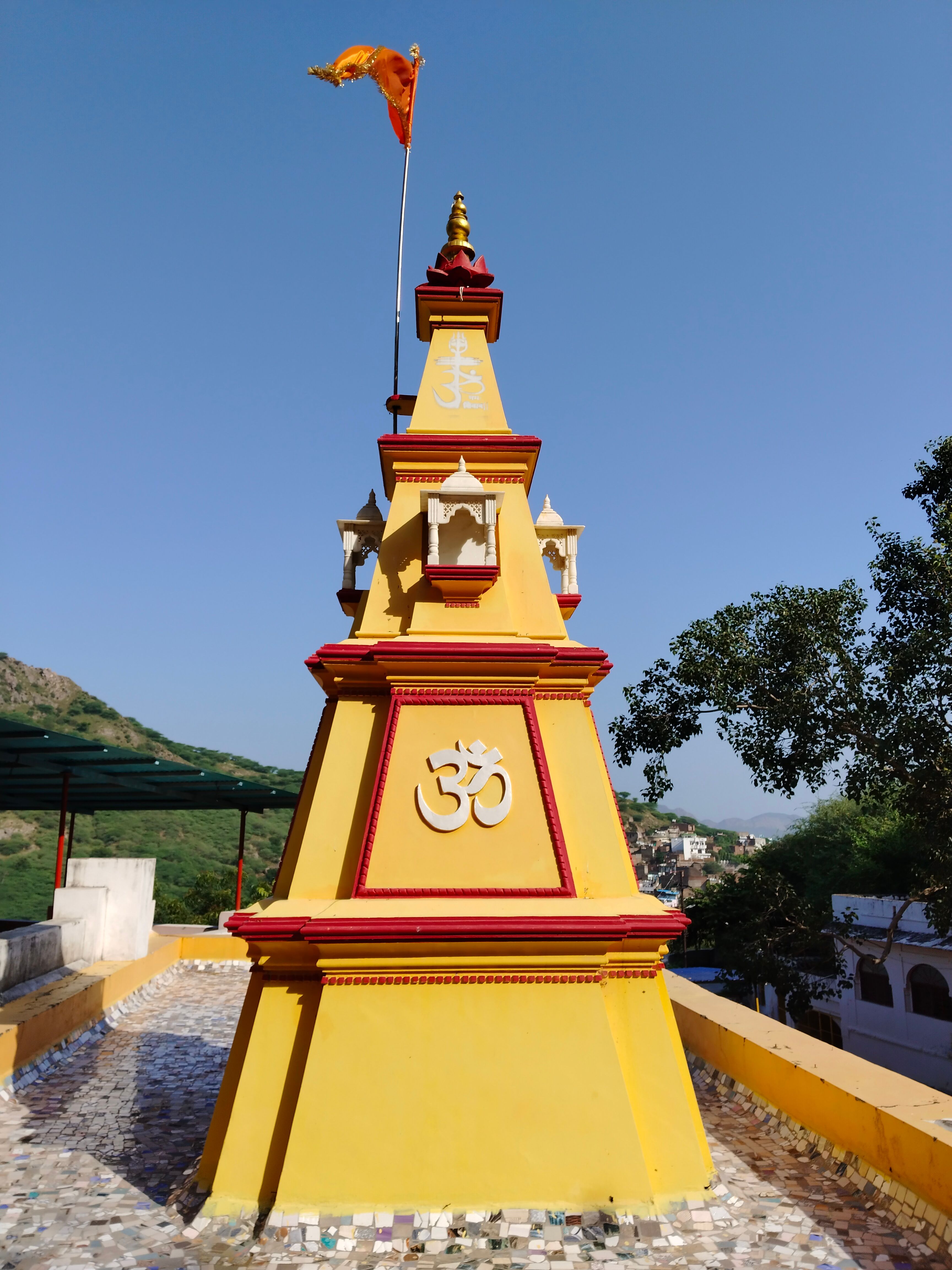 Bright yellow temple structure with an Om symbol and a flag waving on a sunny day.