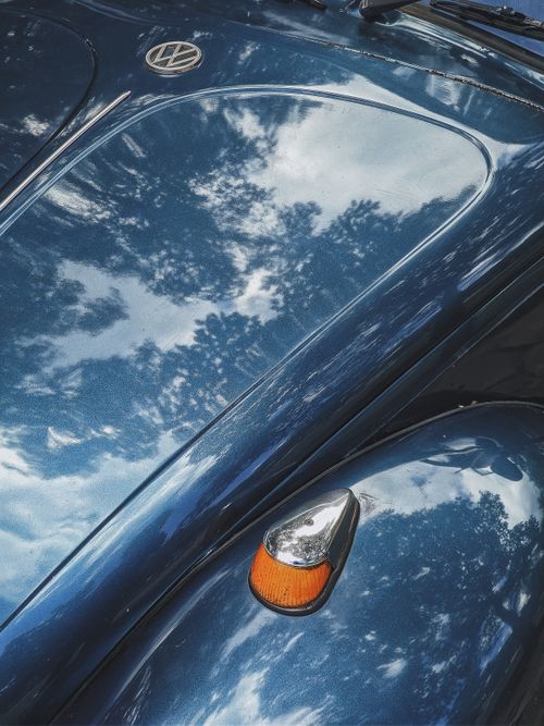 Free Close-up of a classic Volkswagen Beetle hood reflecting the sky and trees, showcasing vintage design. Stock Photo