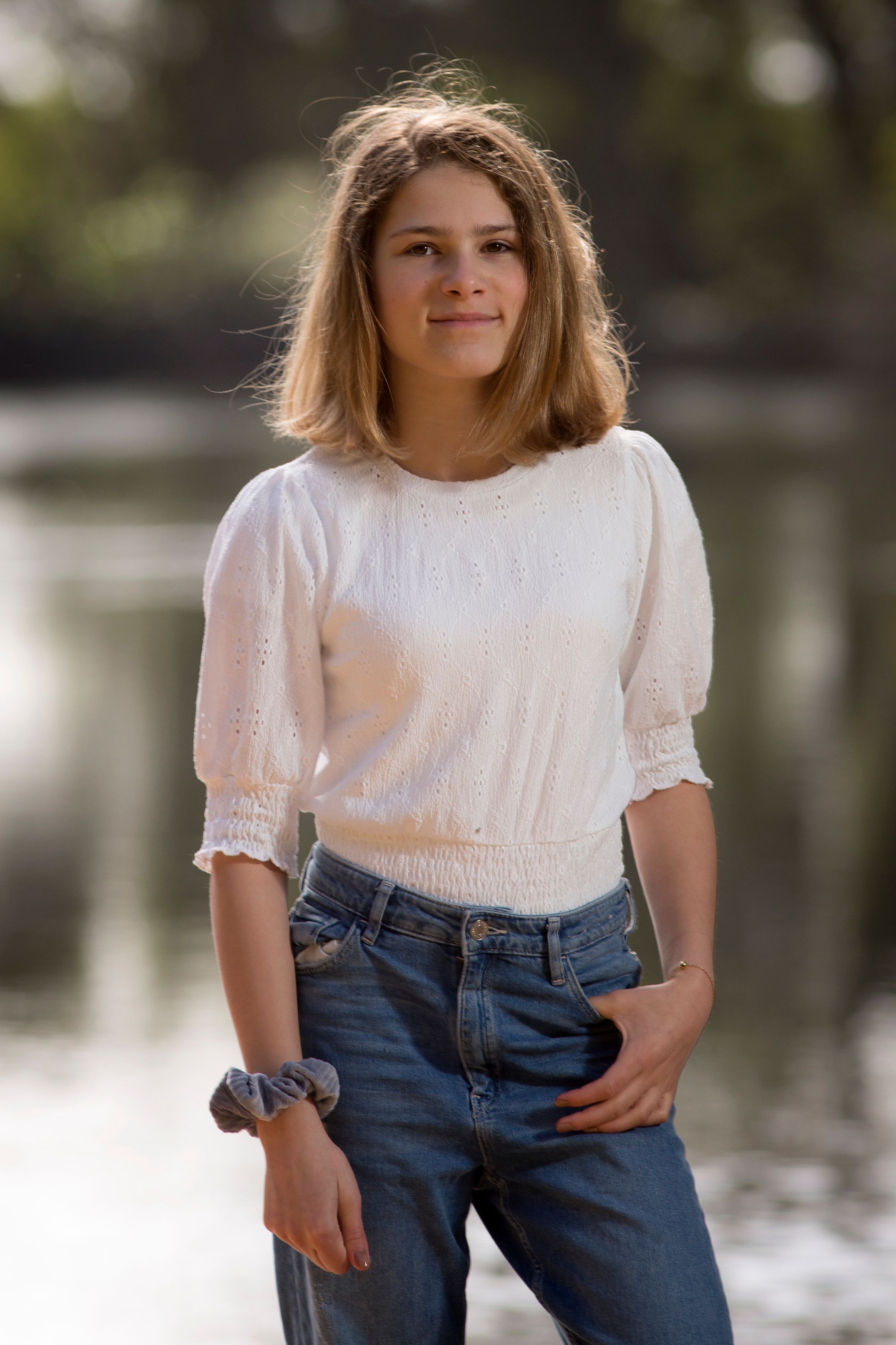 Casual portrait photo of a young woman wearing a white blouse and jeans by a river.