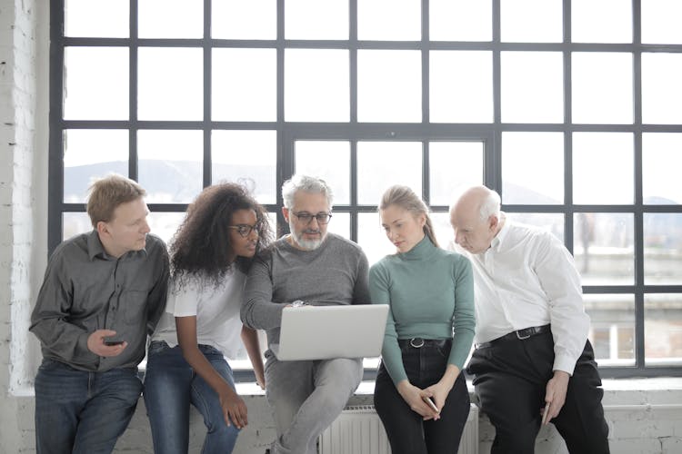 Group Of People Sitting By The Window And Looking At A Laptop