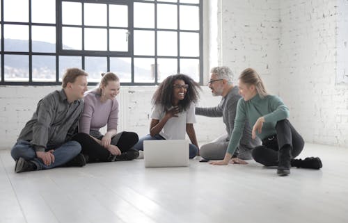 Diverse friends conversing while using laptop and sitting on floor