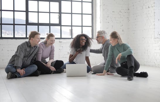 A group of diverse adults sitting indoors, enjoying time together using a laptop and communicating.