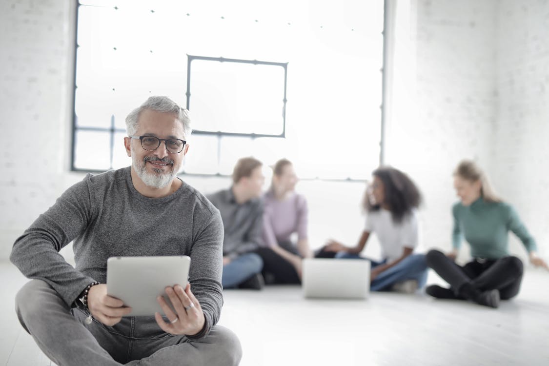 Group Of People Sitting On The Floor With Focus On Man Holding A Digital Tablet