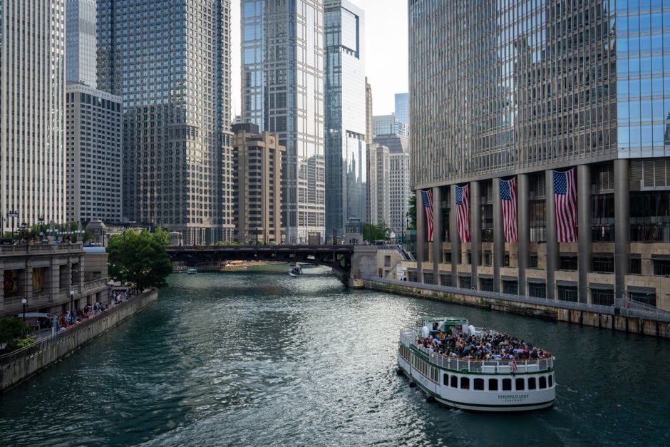 A boat navigates the Chicago River surrounded by skyscrapers and city architecture.