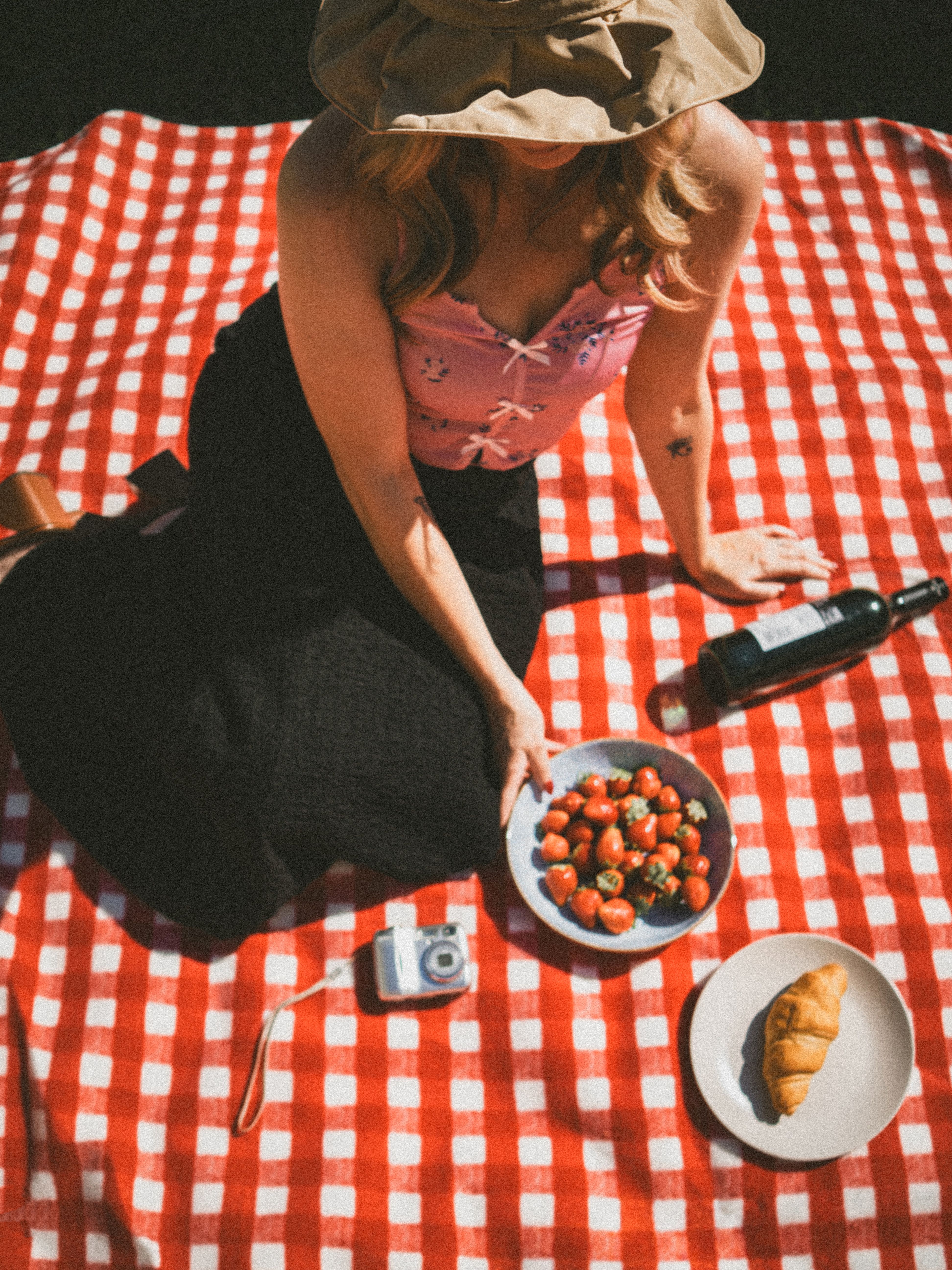 Woman enjoying a summer picnic with wine and strawberries on a red checkered blanket.