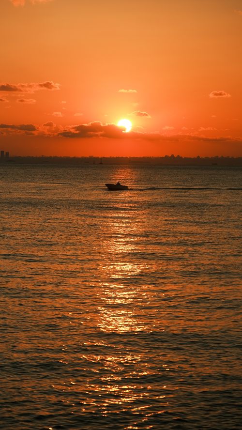 Free A serene sunset over ocean waters with a boat silhouette, capturing a peaceful evening scene. Stock Photo