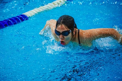 Free A focused female swimmer competing with the butterfly stroke in a blue pool. Stock Photo