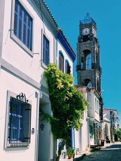 Free Picturesque street with historic clock tower in Bozcaada, surrounded by vibrant architecture. Stock Photo