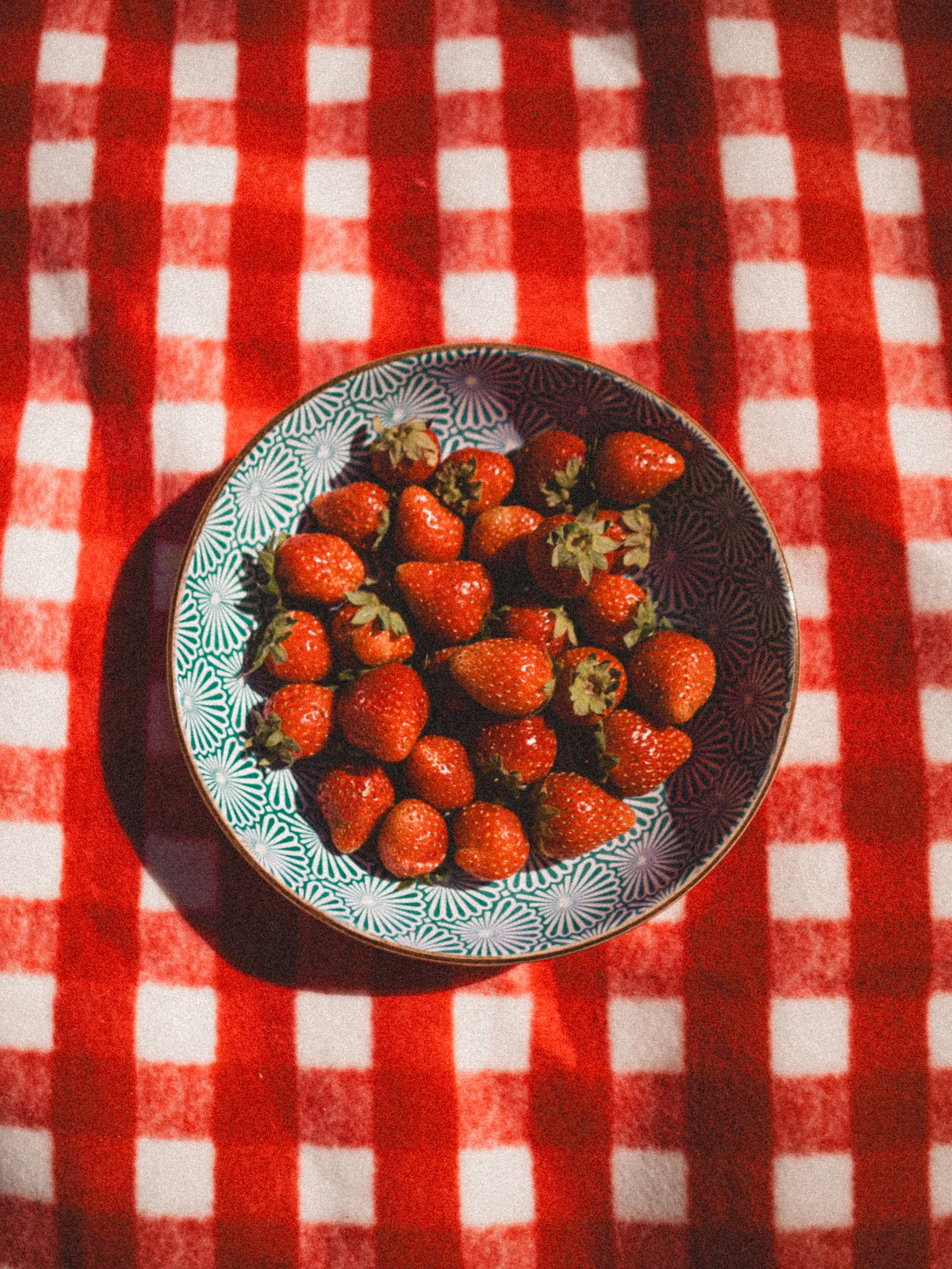 A bowl filled with ripe strawberries on a red checkered cloth, perfect for summer themes.