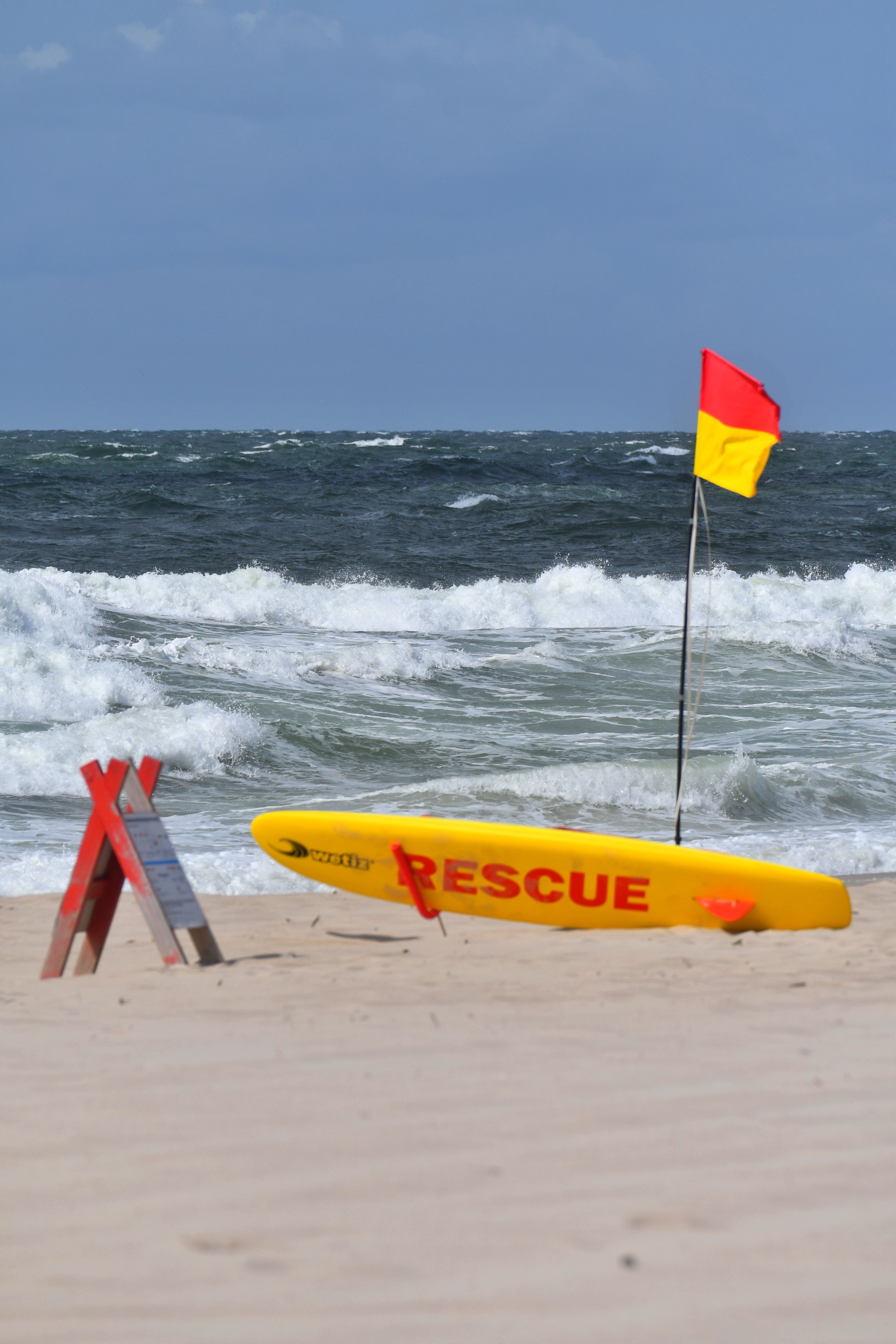 Gele reddingsplank en veiligheidsvlaggen op een zandstrand met golven.