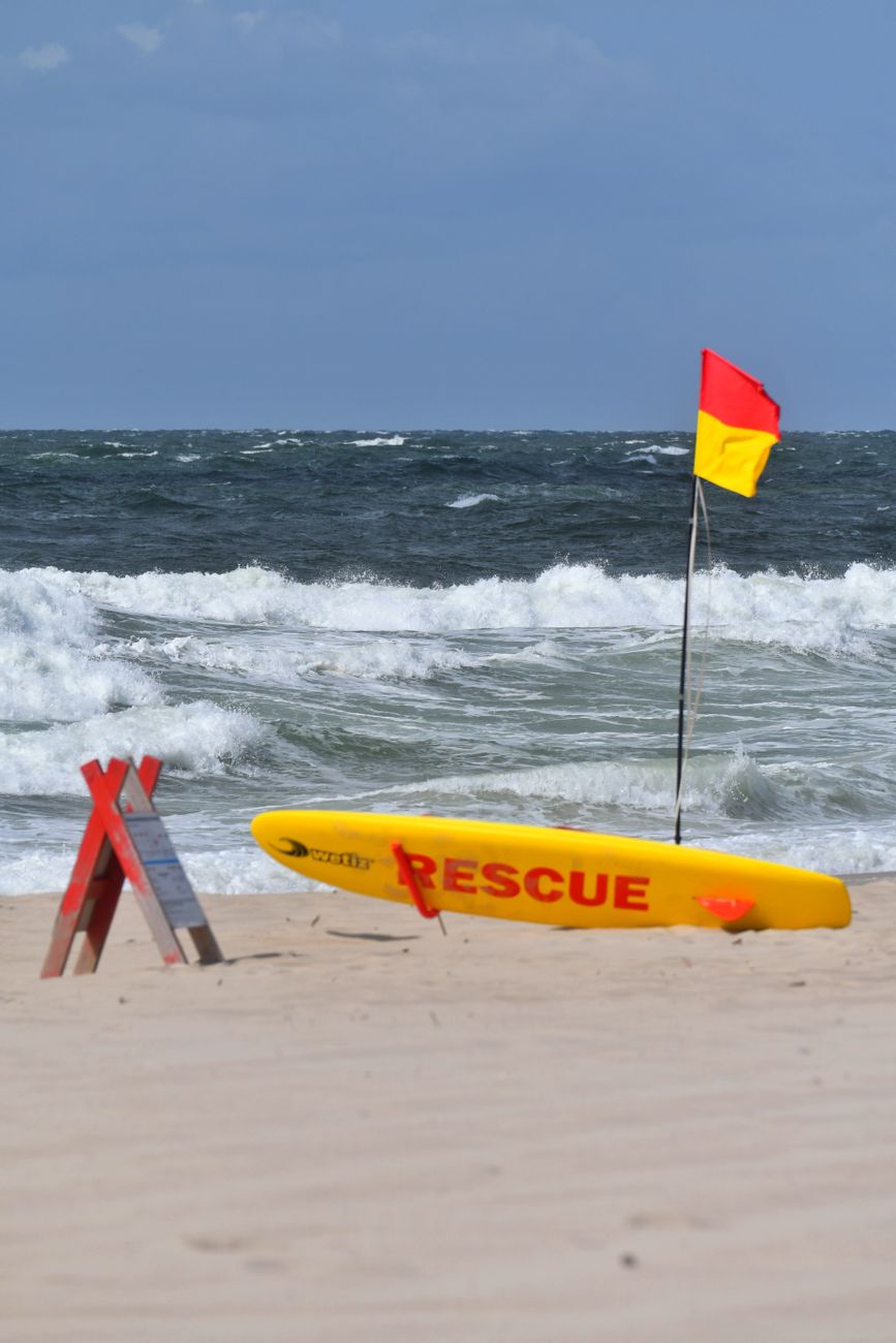 Gele reddingsplank en veiligheidsvlaggen op een zandstrand met golven.