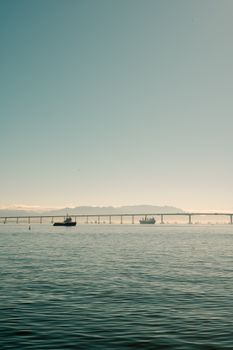 Tranquil water scene with a boat and distant bridge under a clear sky.