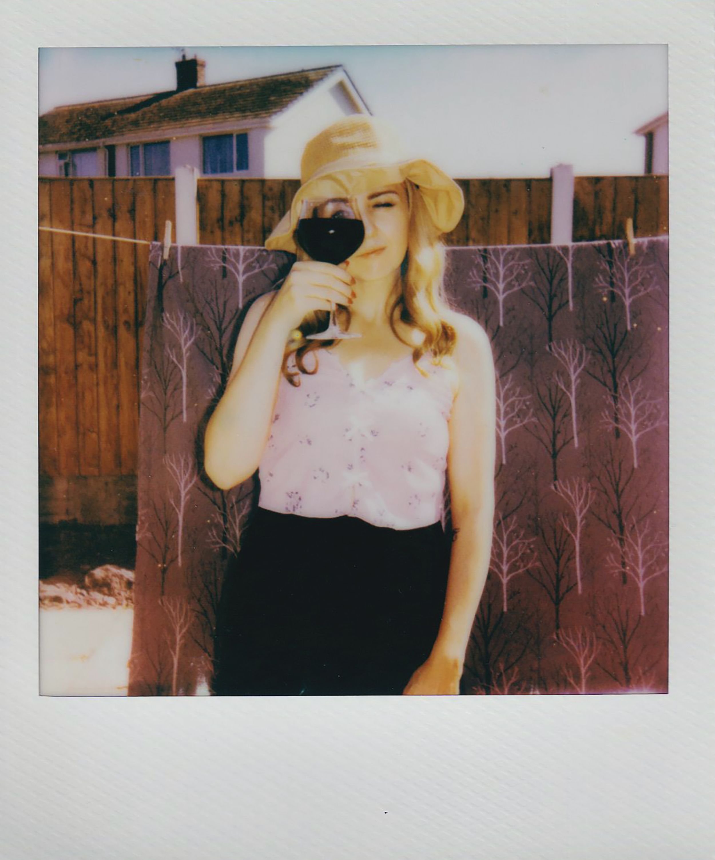 A woman in a sunhat enjoying a glass of red wine outdoors on a sunny summer day.