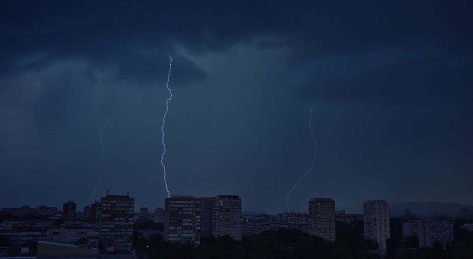A city skyline at night with dramatic lightning bolts striking the sky during a storm.