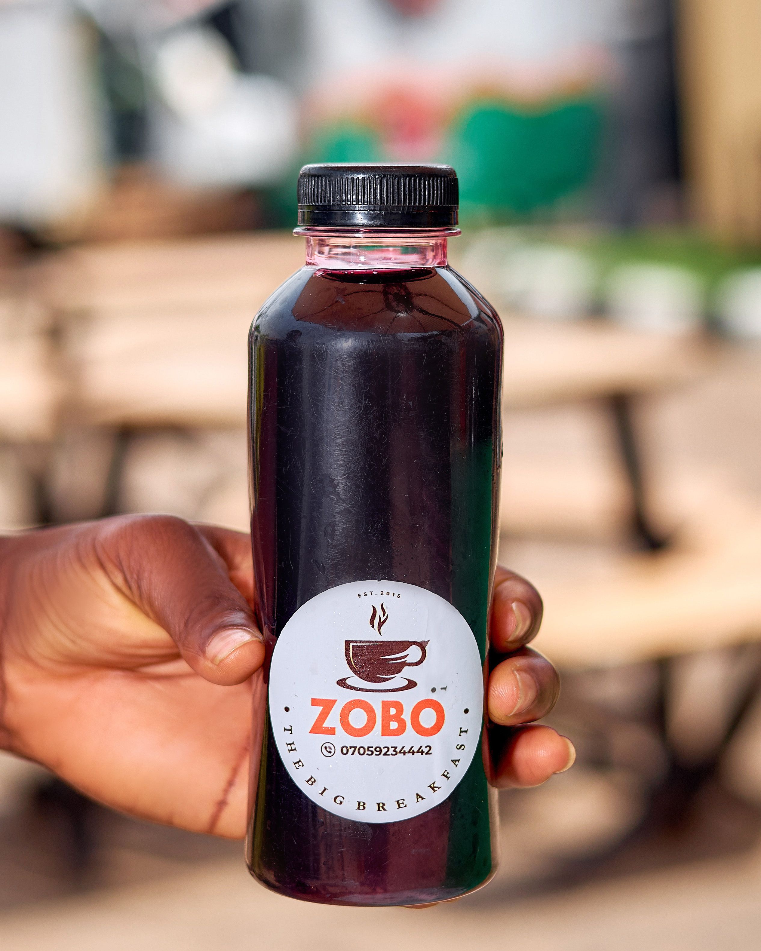 Hand holding a bottle of refreshing Zobo drink outdoors, perfect for a sunny day.