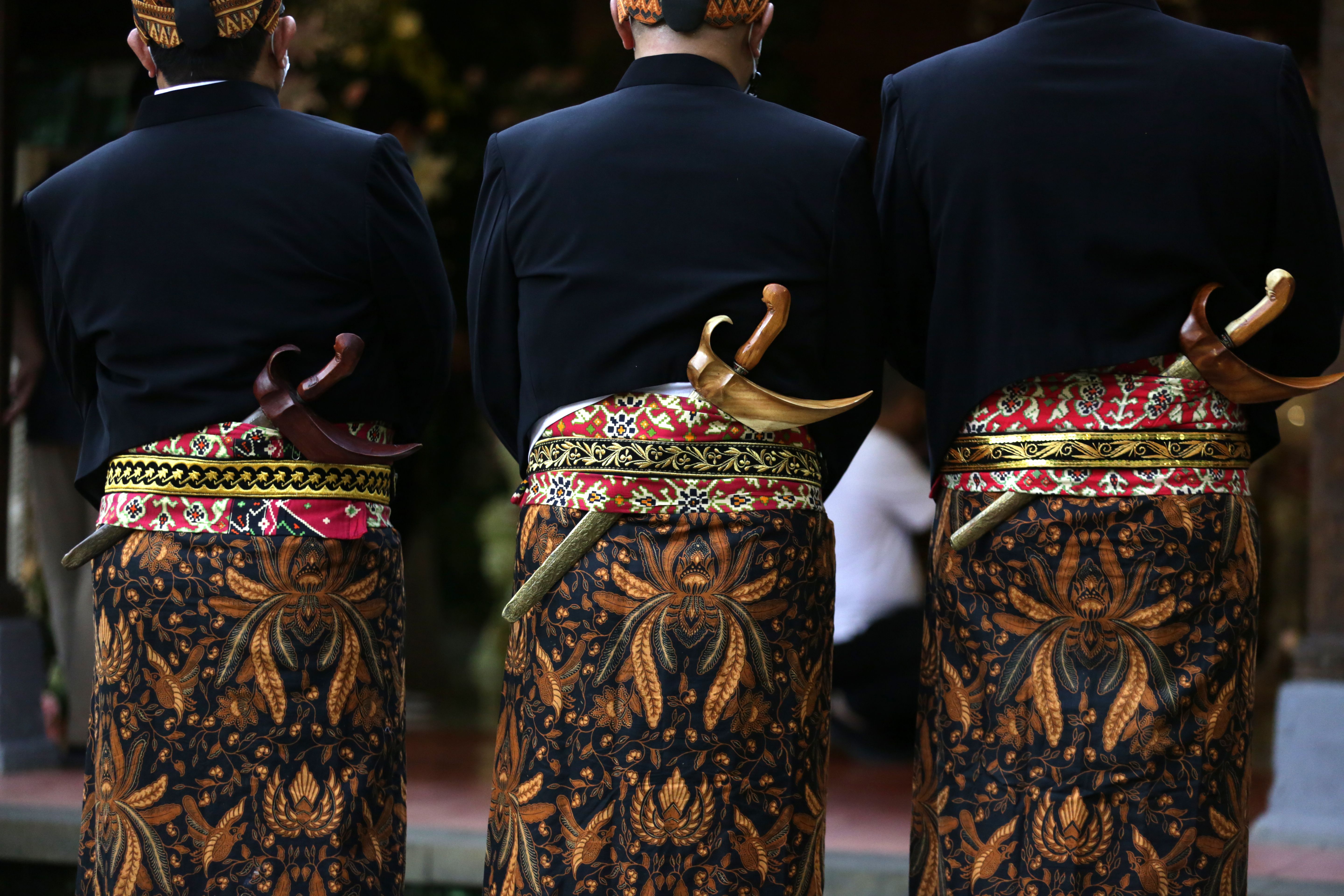 Men in Javanese attire with kris daggers at a traditional ceremony.