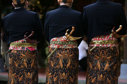 Men in Javanese attire with kris daggers at a traditional ceremony.