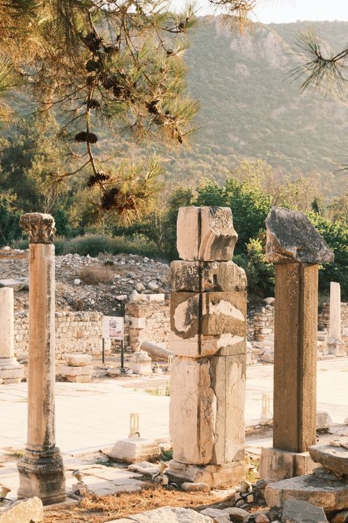 Free Sunlit ancient columns in an archaeological site surrounded by mountains and trees. Stock Photo