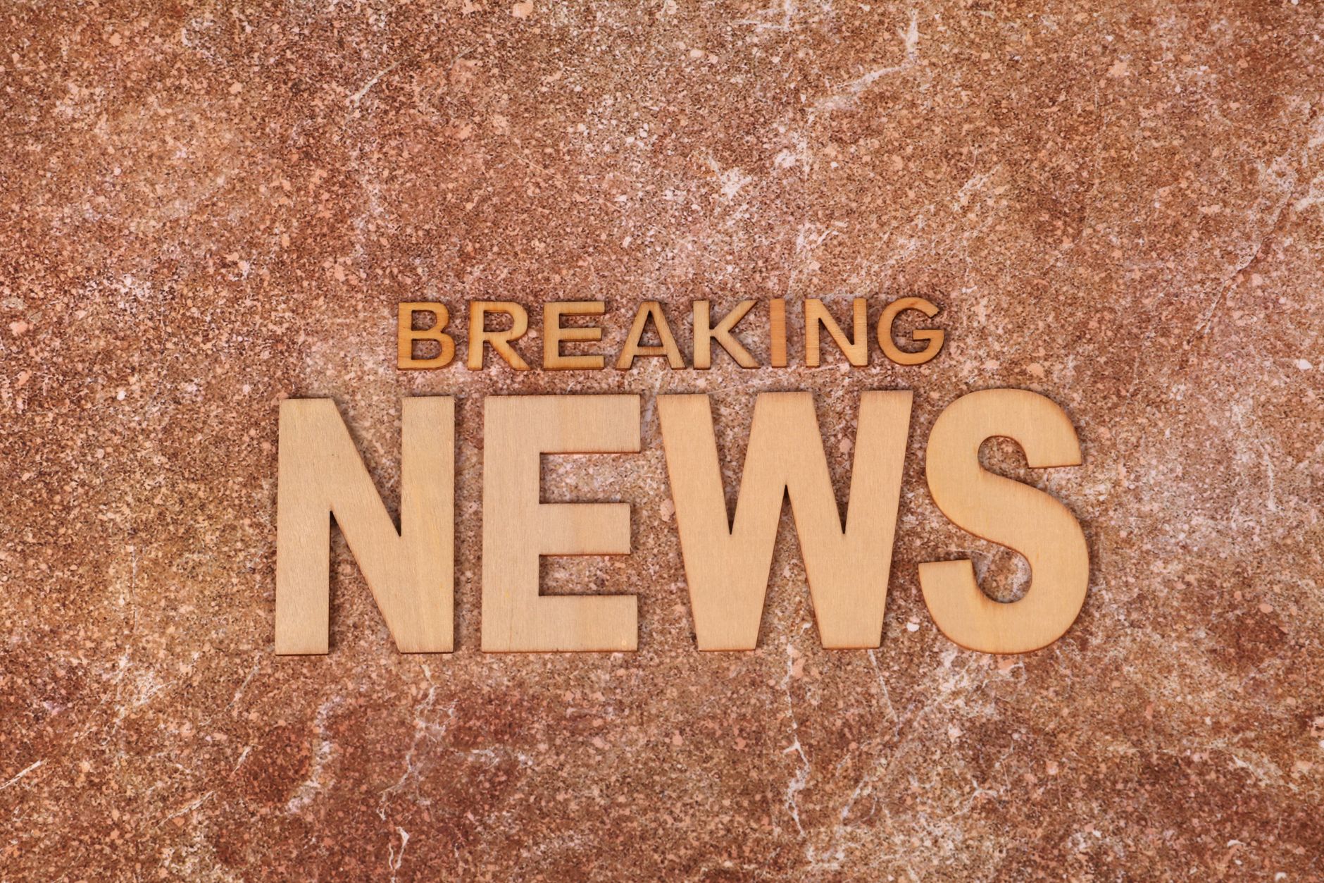 Wooden letters spell 'Breaking News' on a textured, marble-like background. Ideal for newsworthy content.