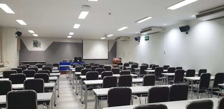 Spacious empty conference room with neatly arranged tables and chairs, ready for a meeting or class.
