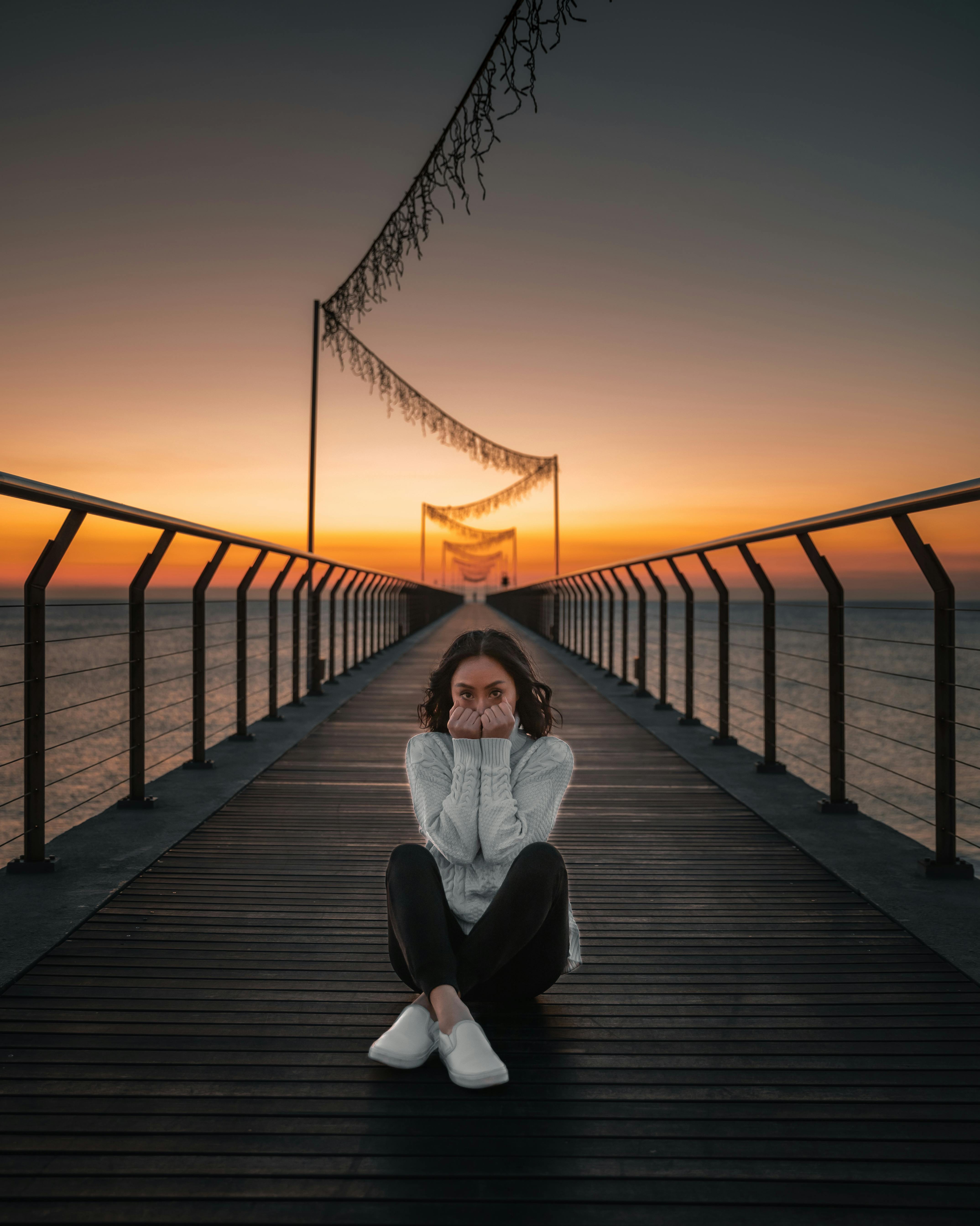 woman in white long sleeve shirt sitting on wooden dock during sunset