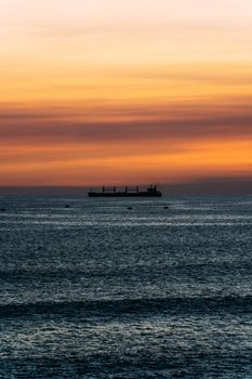 A serene sunset over the ocean with a silhouette of a cargo ship in the distance, creating a peaceful atmosphere.