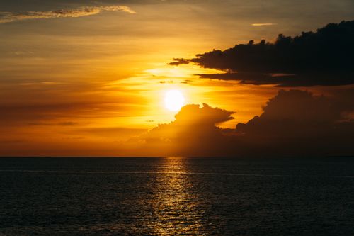 Free A mesmerizing sunset with vibrant orange and yellow hues reflected on the calm ocean surface. Stock Photo