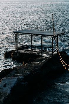 Serene coastal view with metal structure on rocks, bathed in sunset light over the ocean.