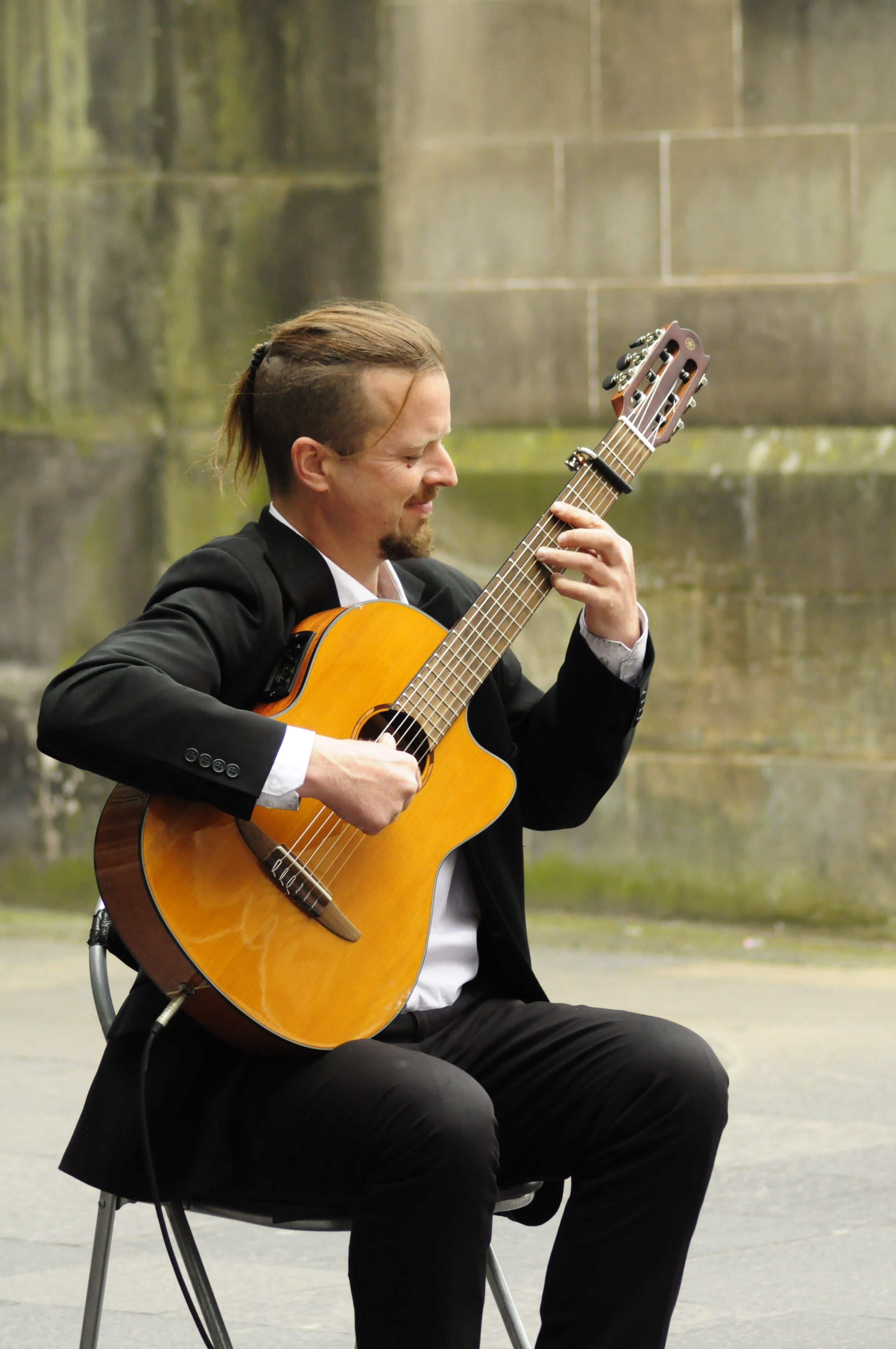 Acoustic guitarist performs on Edinburgh's Royal Mile, captivating passersby with classical tunes.